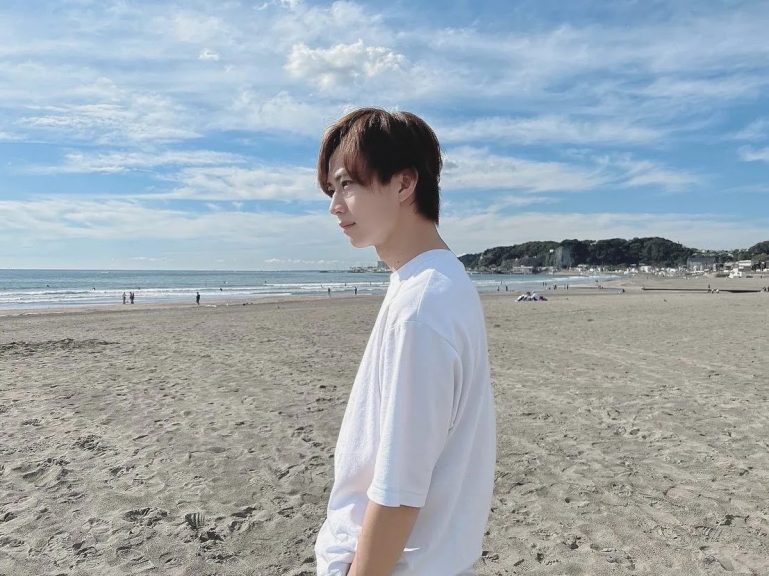 青い空、白い砂浜。白いTシャツを着た爽やかな青年が左の遠くを見つめている。