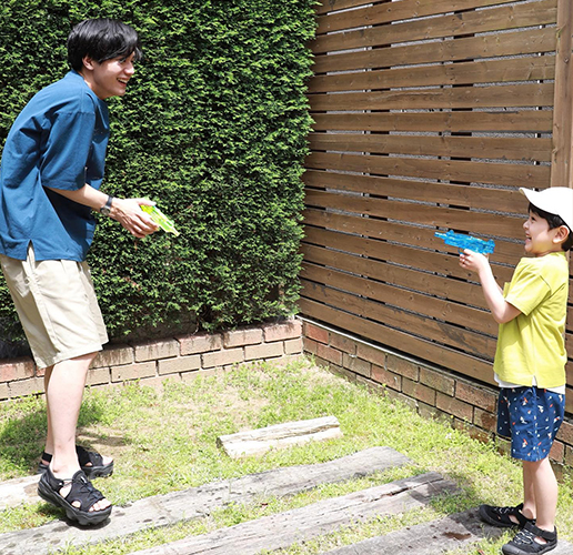 綺麗に整備された庭らしき場所で、小さな男の子と20代らしき男性が水鉄砲で遊んでいる。とても楽しそうである。